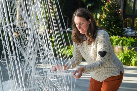A person arranging white geometric forms and string into the shape of a tree. 